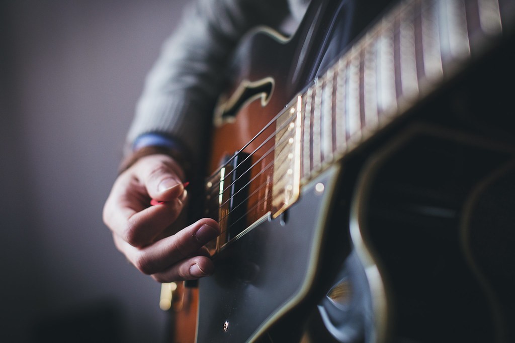 Close-up of a hand playing electric guitar strings with a pick